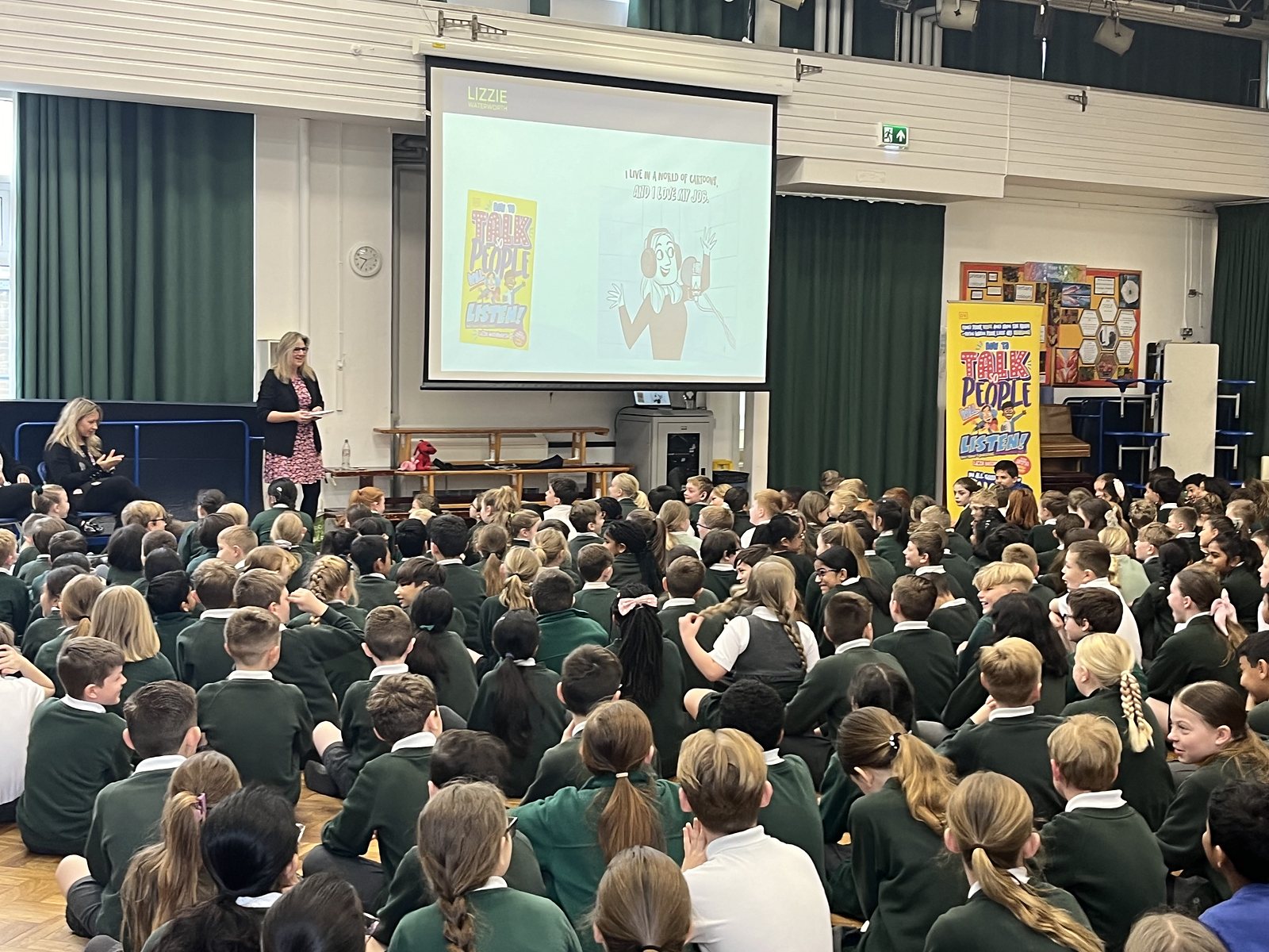 Lizzie presenting a whole-school assembly to a packed hall of children
